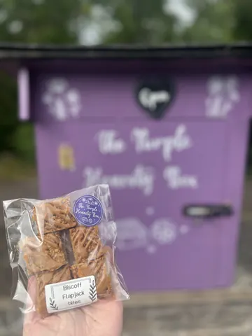 A person is holding a bag of cookies in front of a purple building.