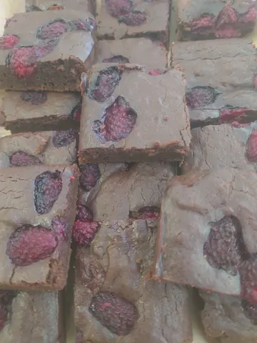 A stack of brownies with red raspberries on top.