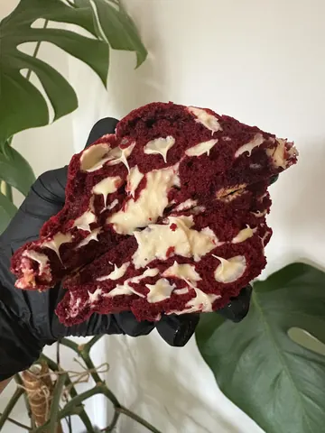 A hand holding a piece of red cake.