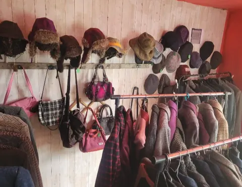 A wall with a shelf full of hats and purses.