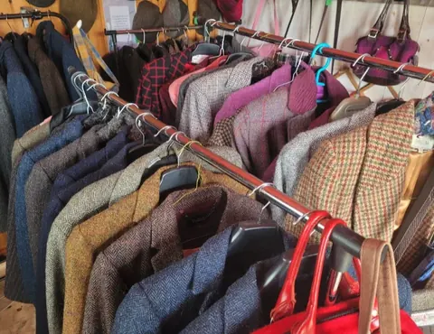 A rack of clothes with a red purse hanging on the side.
