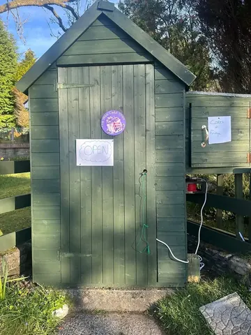 A small green shed with a purple sign on it.