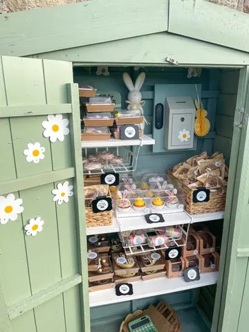 A small green building with a white door and a shelf full of food.