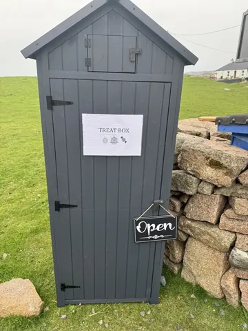 A small grey shed with a sign that says open.