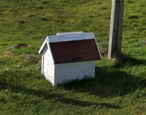 A small white shed with a red roof.