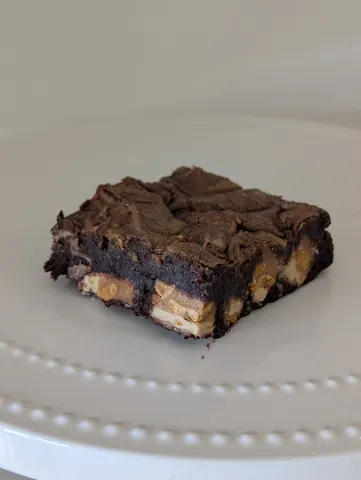 A square piece of chocolate cake on a white plate.