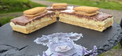 A cow is on a table with a plate of food.